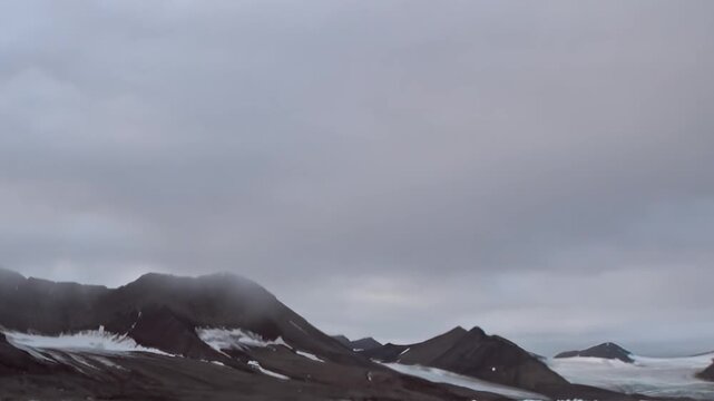 A steep mountain slope rises into fog above cold coastal water. The broader composition includes snow, wide framing and low clouds, keeping surface texture and scale clearly readable.