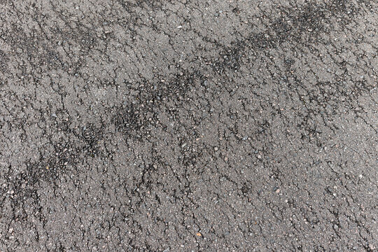 Close-up of cracked asphalt road texture with worn pavement, loose gravel and weathered surface details ideal for backgrounds, construction, repair, urban design and texture reference imagery
