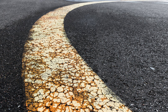 Close-up of a curved, cracked yellow road line on rough asphalt showing weathered paint, texture and urban decay; evokes age, wear, direction and abstract patterns for design or editorial use