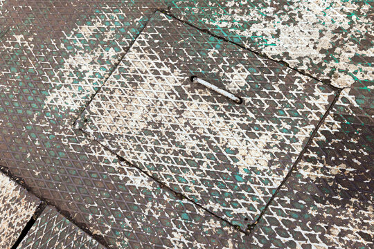Close-up of a weathered metal manhole cover showing diamond plate pattern, chipped white and green paint, rusted handle and gritty urban texture, suitable for industrial, grunge infrastructure themes