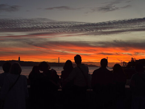 People watching a dramatic sunset over 25 de Abril Bridge in Lisbon, Portugal