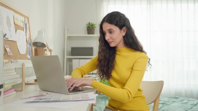 Latino female college student typing on laptop in university dormitory. 