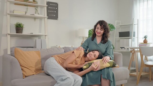 Senior Latino mother relaxing on sofa with adult daughter resting on her lap.