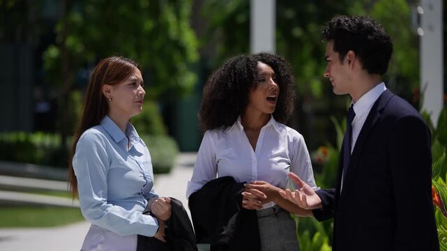 Three young professionals swap ideas in the open air with coffee, the camera close enough to catch every expression as the discussion moves around the little circle