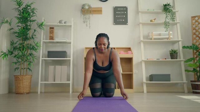 African Black plus-size woman rolling out yoga mat before workout. 