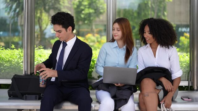 Laptop balanced on the knee at a covered bench, three professionals sharing one screen while they wait, flexible working wherever the day happens to put the team