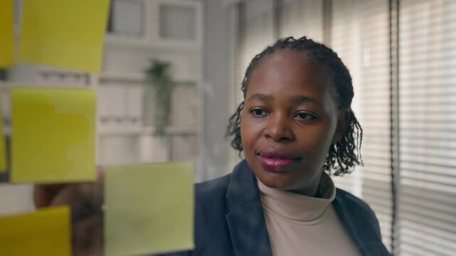 African plus-size female placing sticky note on board in conference room. 