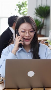 Asian Businesswoman Celebrating Success on Phone Call with Laptop in Office