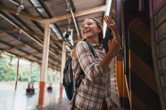 Happy backpacker waving goodbye from a train at station
