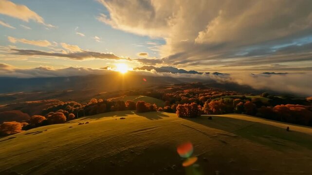 Golden sunrise over misty mountain valley as drifting clouds reveal rolling green hills and autumn trees in warm morning light, cinematic aerial landscape footage of rural countryside