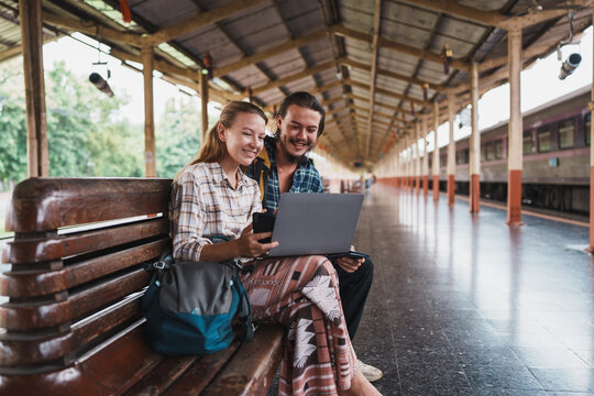 Backpackers couple using laptop and phone at railway station