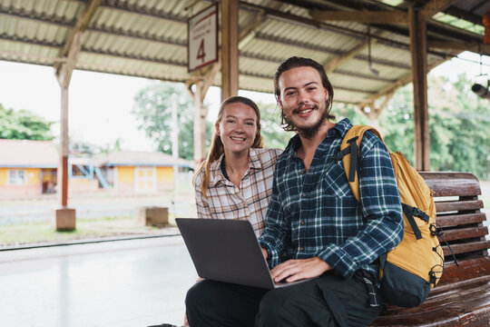 Backpackers smiling working with laptop at railway station