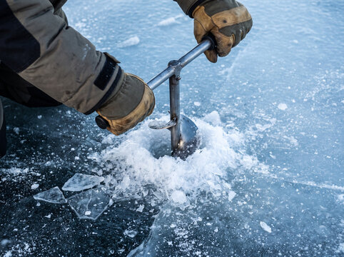 Person ice fishing and drilling a hole in frozen lake  