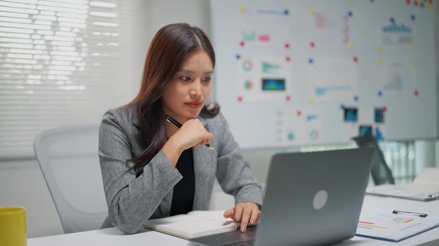Young professional woman using a laptop at a desk in a modern office, focused on business planning, productivity, strategy, and corporate work.