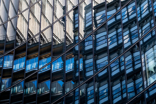 Modern facade with blue windows and external structural elements creates a layered geometric pattern of contemporary urban architecture and reflections.