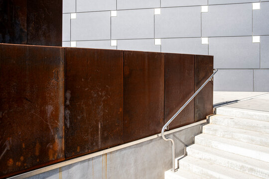 Minimalist concrete stairway beside a weathered steel wall creates strong lines, texture and geometric contrast within contemporary urban architecture.