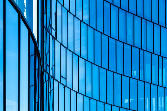 Blue glass curtain wall with repeating vertical lines and reflections forms a minimalist abstract pattern across a contemporary building facade.