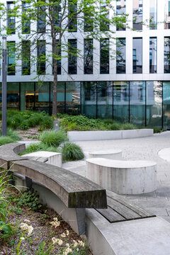 Landscaped urban courtyard with concrete seating, ornamental planting and a modern glass building combines greenery, public space and contemporary architecture.