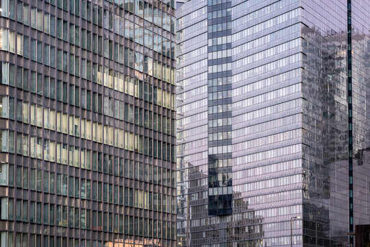 Reflective glass facades on modern towers create layered vertical grids, windows and architectural patterns in a dense contemporary urban setting.