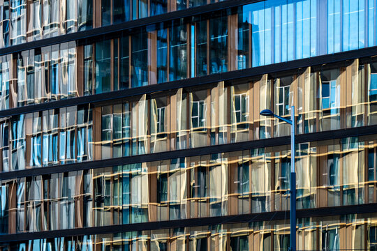 Modern glass facade with repeating windows and layered reflections creates a dense architectural pattern across a contemporary urban building exterior.
