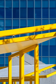Bright yellow structural beams contrast with a blue glass facade, forming a bold geometric composition of color, lines and contemporary urban architecture.
