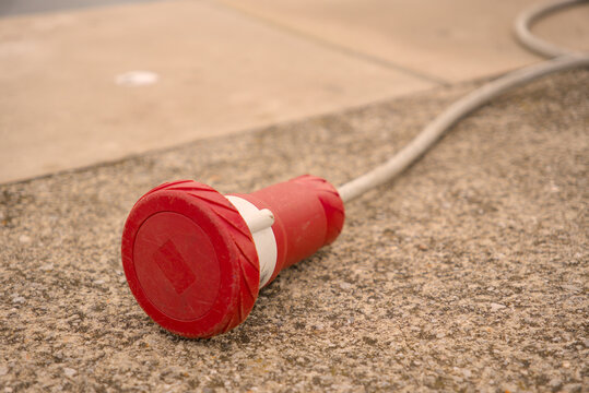 Red industrial CEE electrical plug on a concrete pier in Rijeka harbor, Croatia. Marine shore power connection detail.