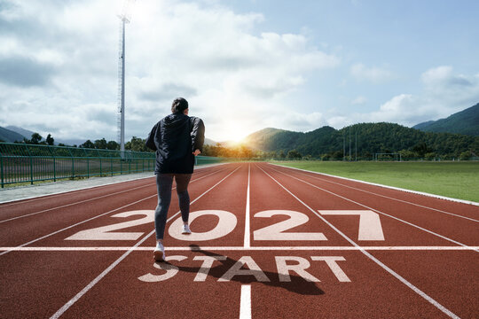 New year resolution 2027 concept. Word start 2027 on athletics track and athlete woman runner preparing to new year at sunset for challenge and beginning planning health and the goal to success.