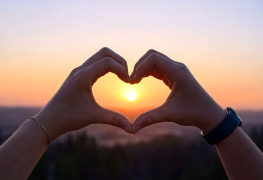 Silhouette of hands forming a heart shape in front of a beautiful sunset sky with warm colors