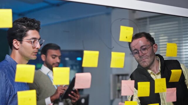 Business Team Brainstorming Ideas on Glass Wall with Sticky Notes