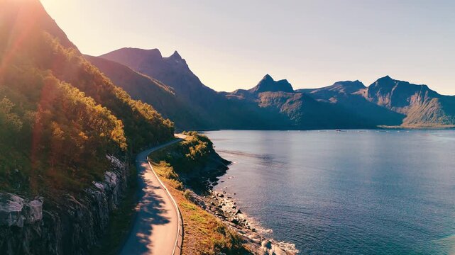 Cinematic forward aerial drone shot following a scenic coastal mountain road with an oncoming car during golden hour sunlight in Norway
