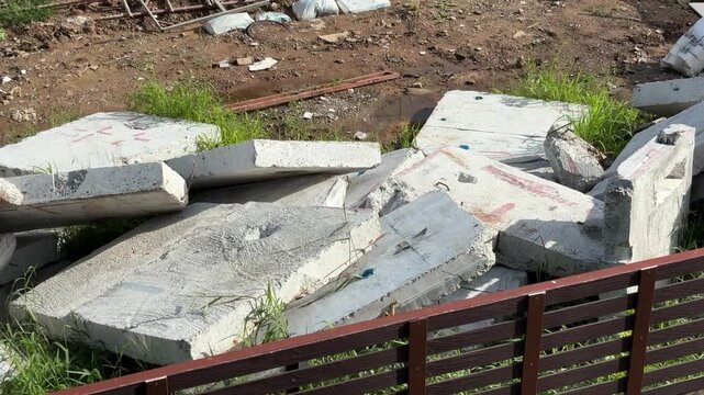 Broken concrete wall on the ground outdoors during daylight, showing visible cracks, damage, and deteriorated construction material.