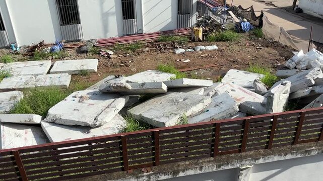 Broken concrete wall on the ground outdoors during daylight, showing visible cracks, damage, and deteriorated construction material.