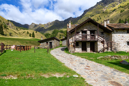 Rustic stone cottages and a winding cobblestone path in Case di Viso, a traditional alpine village near Ponte di Legno in Lombardy, Italy.