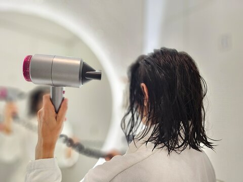 Person using a hair dryer while looking into a mirror at a bathroom concept