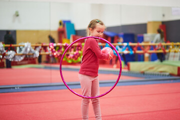 Girl practicing rhythmic gymnastics with a hoop and ball in an indoor gym decorated for the winter holidays © Ekaterina Pokrovsky