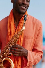 Fototapeta premium Stylish male saxophonist wearing an orange scarf playing a golden saxophone outdoors for music poster and portrait banner