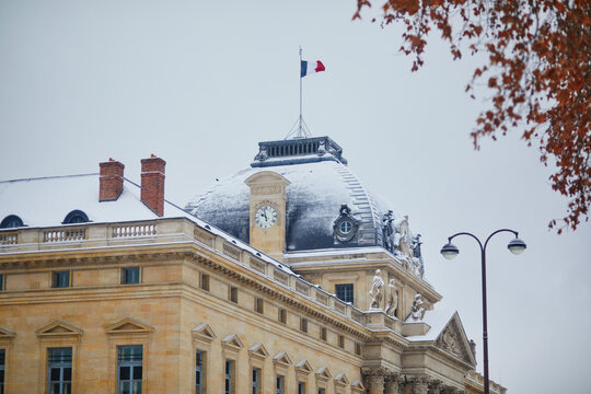 Snow-covered Ecole Militaire with French flag on dome in Paris during winter.