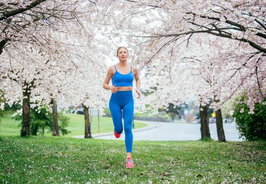 White woman running through park with blooming cherry blossom trees