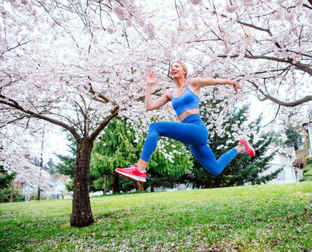 White woman jumping in athletic wear under blooming cherry blossom