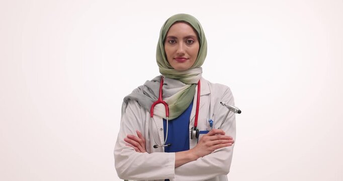 Muslim neurologist holds specialized neurological reflex hammer. Smiling doctor in hijab poses confidently in medical office against white background