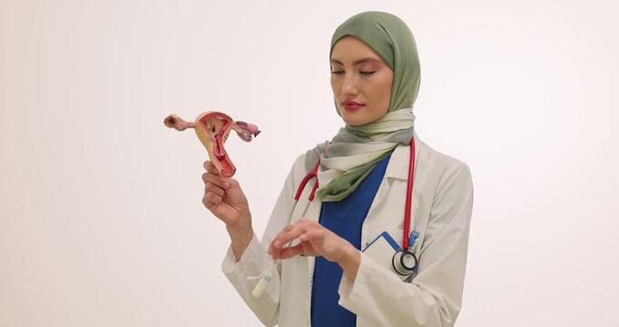 Female gynecologist explains correct and hygienic use of tampon. Physician in hijab shows detailed anatomical model of uterus to students at lesson