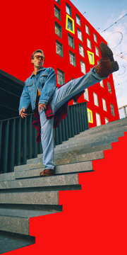 Stylish young man performs high kick on city stairs with bold red graphics and rebellious attitude. Street fashion, youth culture and urban expression concept.
