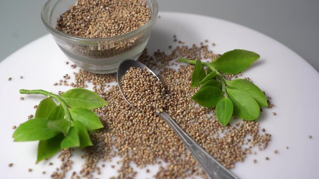 Raw Hemp Seeds or Cannabis sativa seeds displayed in a glass bowl with a spoon and fresh green leaves on a white background top view