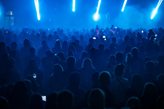 Silhouettes of crowd enjoying blue lights and stage illumination during night 