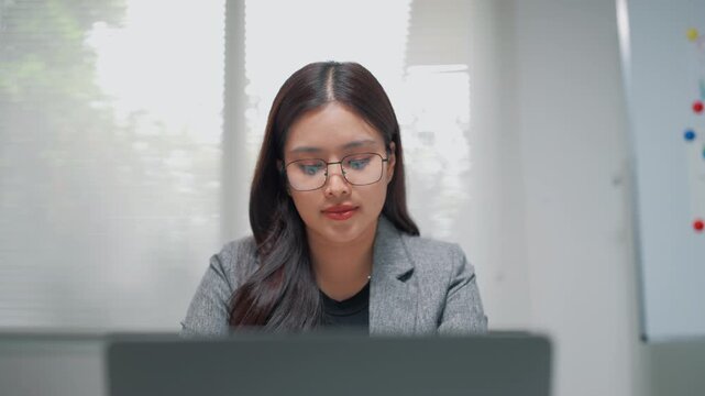 Young professional woman in glasses concentrating on laptop work in a modern office, representing business, planning, productivity, and corporate focus.