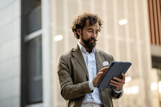 Confident businessman using digital tablet in front of modern office building