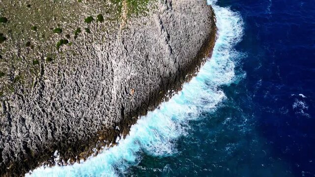 Aerial drone zoom out above rugged limestone cliffs and powerful sea waves along the Adriatic coastline near Santa Maria di Leuca, Castrignano del Capo, Puglia, Italy.