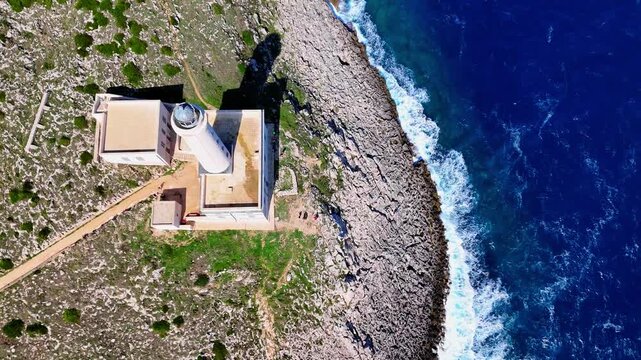 Aerial drone orbit and tilt revealing Santa Maria di Leuca Lighthouse standing on the rocky cliffs of Punta Meliso, overlooking the deep blue Adriatic Sea along the southern coastline of Puglia, Italy