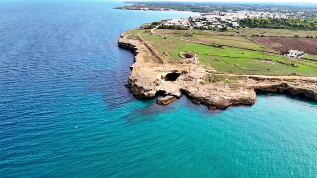 Aerial drone zoom in toward Grotta della Poesia in Roca Vecchia, revealing a natural limestone pool, rocky coastal formations and turquoise Adriatic waters near Melendugno, Puglia, Italy.