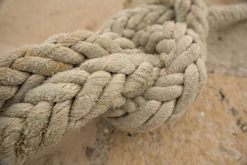Macro close-up of a square knot tied in thick braided mooring rope on a stone quay in Rijeka, Croatia. Nautical knot detail. © YuliiaKettu